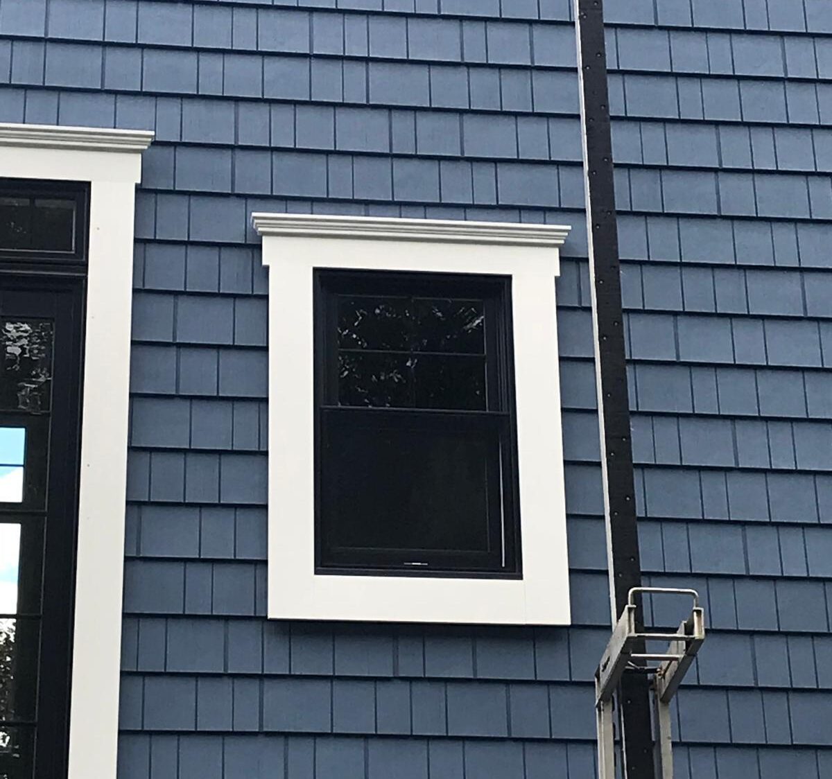 Building exterior with blue siding, black-framed window, white trim, and partial utility structure.