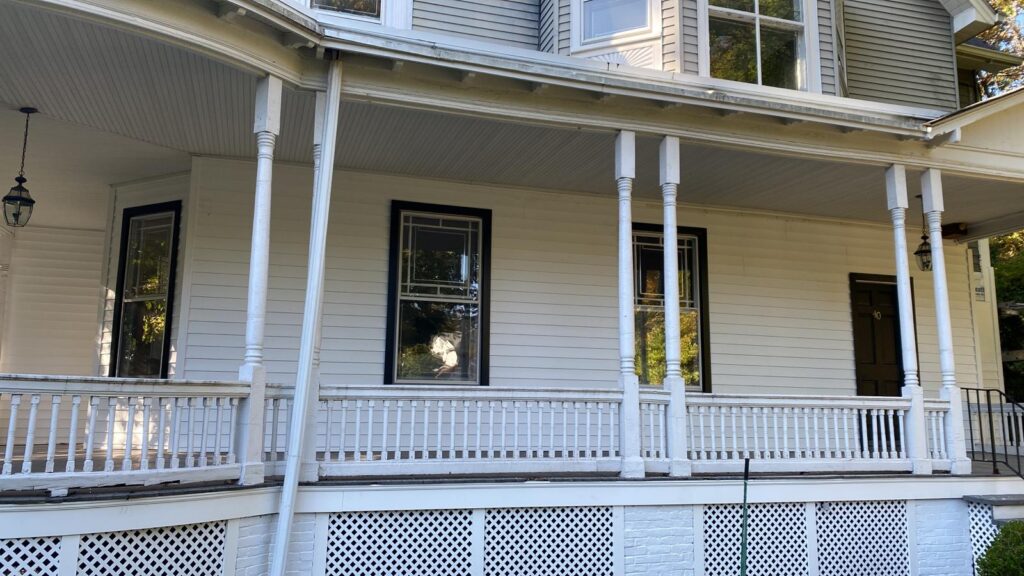White two-story house with wraparound porch, decorative columns, large windows and black door.