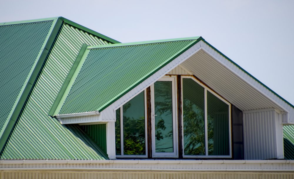 House with green metal roof and gabled dormer, featuring large reflective windows.