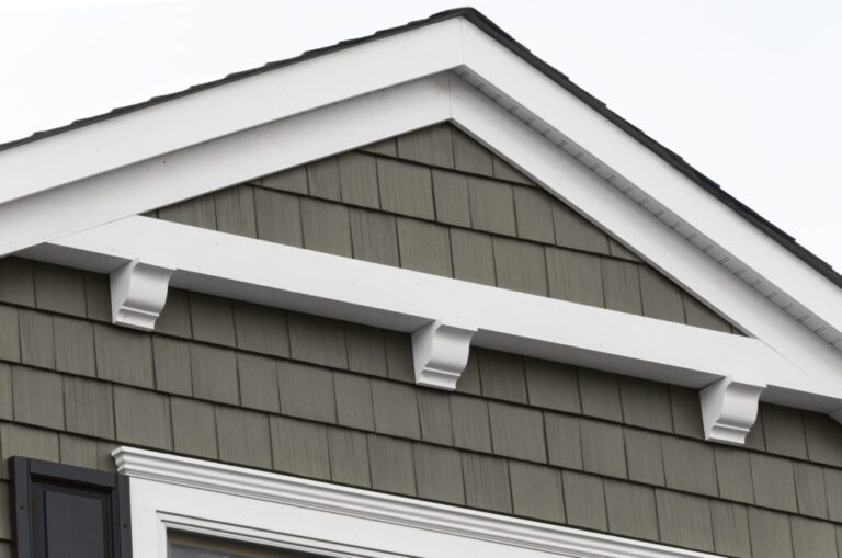 House exterior with gabled roof, greenish-gray siding, white trim, and decorative brackets.