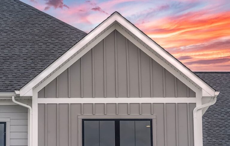 House gable with gray siding, steep asphalt roof, colorful pink and orange sky background.