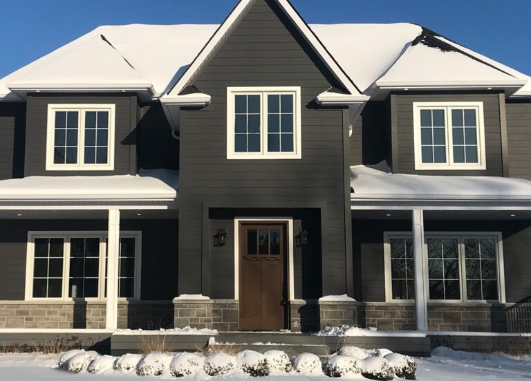 Two-story gray house with white windows and snow-covered roof, central door, white columns.