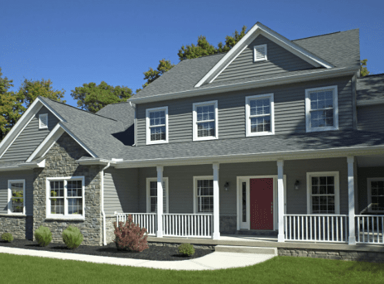 Two-story gray house with stone accents, porch, white railings, peaked roof, and manicured lawn.