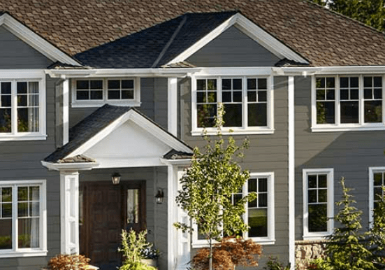 Two-story gray house with white trim, multiple windows, central entrance, trees, and shrubs.