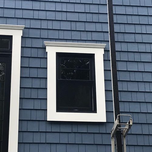 Building exterior with blue siding, black-framed window, white trim, and partial utility structure.